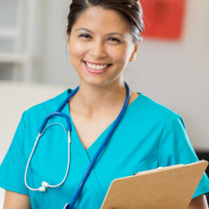 Cheerful mid adult Asian nurse or doctor stands in an exam room. She is wearing scrubs and is holding a patient's medical chart.